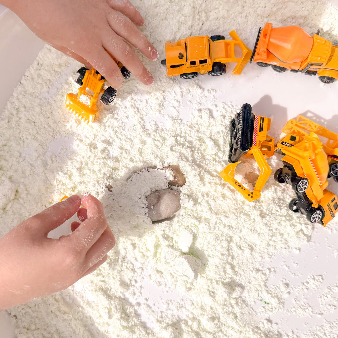 Child playing with fluffy sensory dough, toy diggers and pebbles during a hands-on sensory activity.