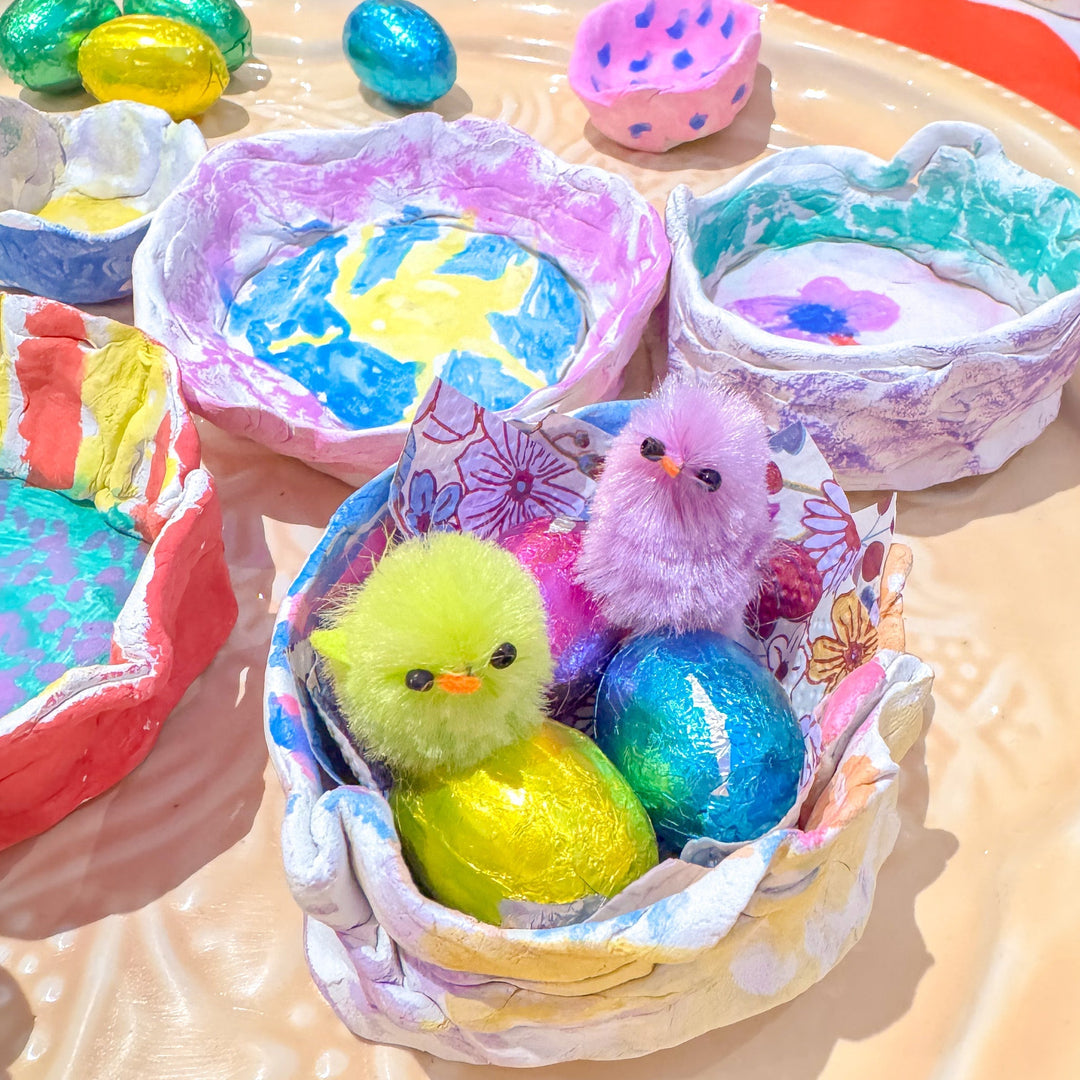 Brightly painted clay Easter nests made by children, decorated with colourful patterns and filled with chocolate eggs and fluffy chicks